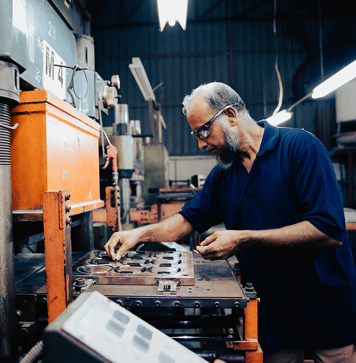 Factory worker with safety glasses and a beard operating a machine press, focused on precision work