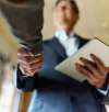 A salesman in a suit shaking hands with another person, holding a tablet, symbolizing a successful business agreement